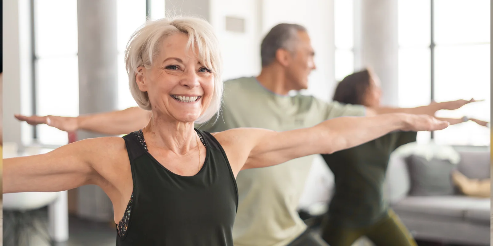 Older adults in a bright yoga class, arms stretched wide and smiling